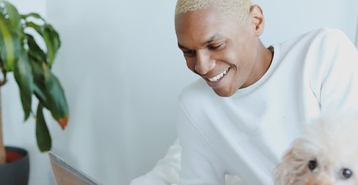 man in white shirt typing at laptop with dog